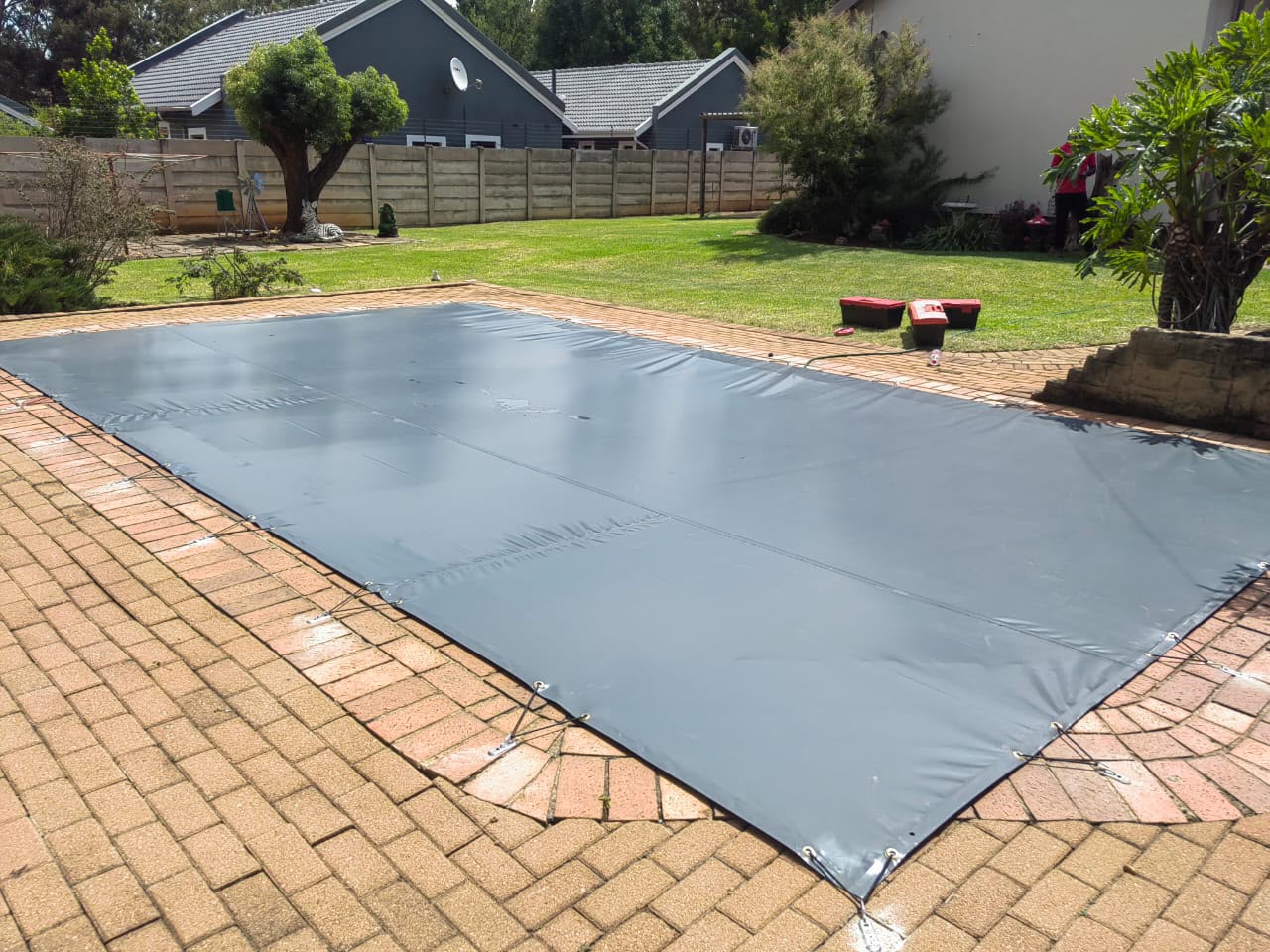 Custom grey PVC cover fitted over a pool on a paved surround